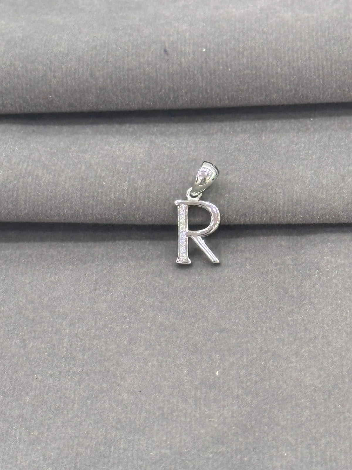 Silver 'R' letter pendant on a gray fabric background