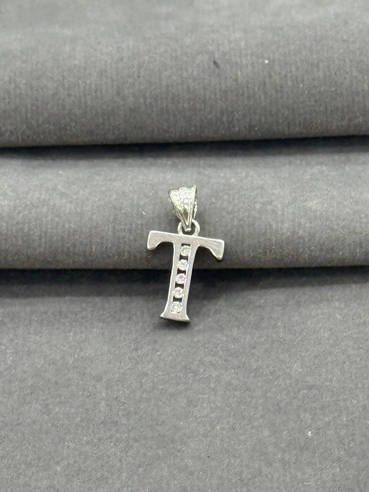 Silver 'T' shaped pendant on a gray fabric background