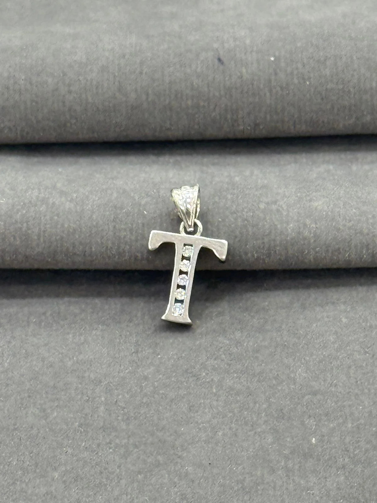 Silver 'T' letter pendant on a gray fabric background