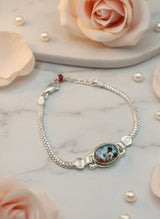 Silver bracelet with a round charm on a marble surface with pink roses and pearls.