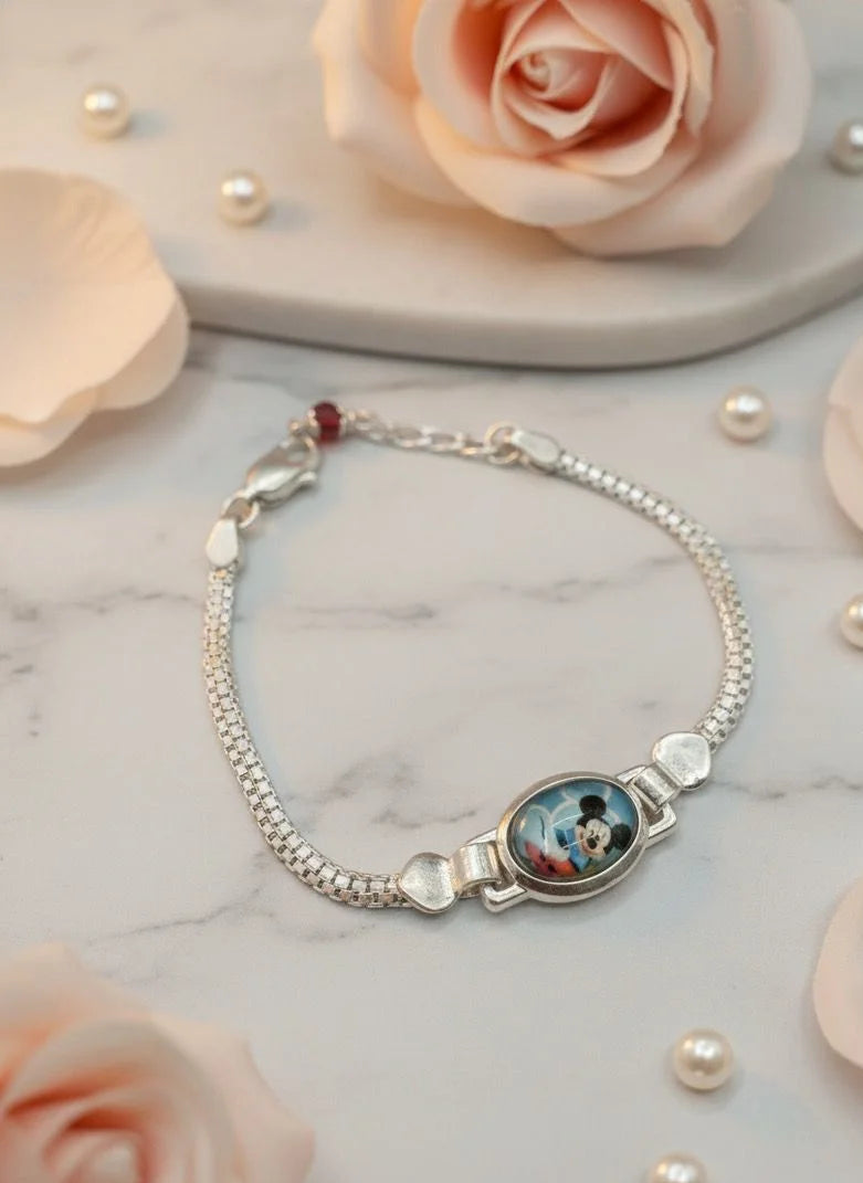Silver bracelet with a round charm on a marble surface with pink roses and pearls.