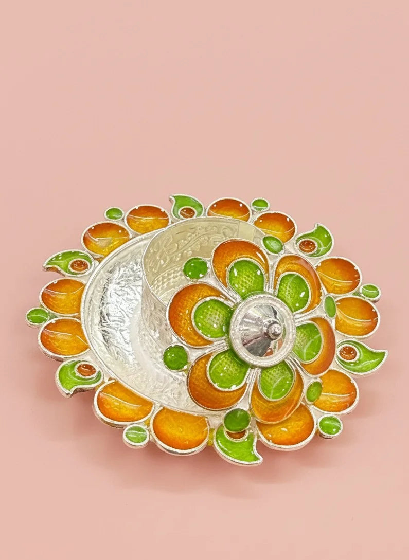 Decorative silver bowl with orange and green floral patterns on a pink background