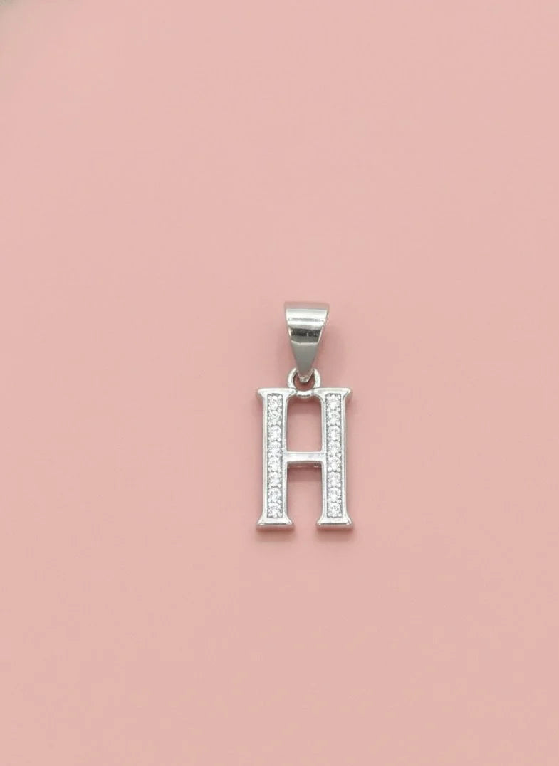 Silver letter 'H' pendant with clear stones on a pink background
