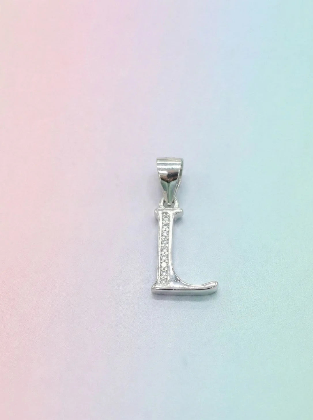 Silver 'L' pendant on a pastel gradient background