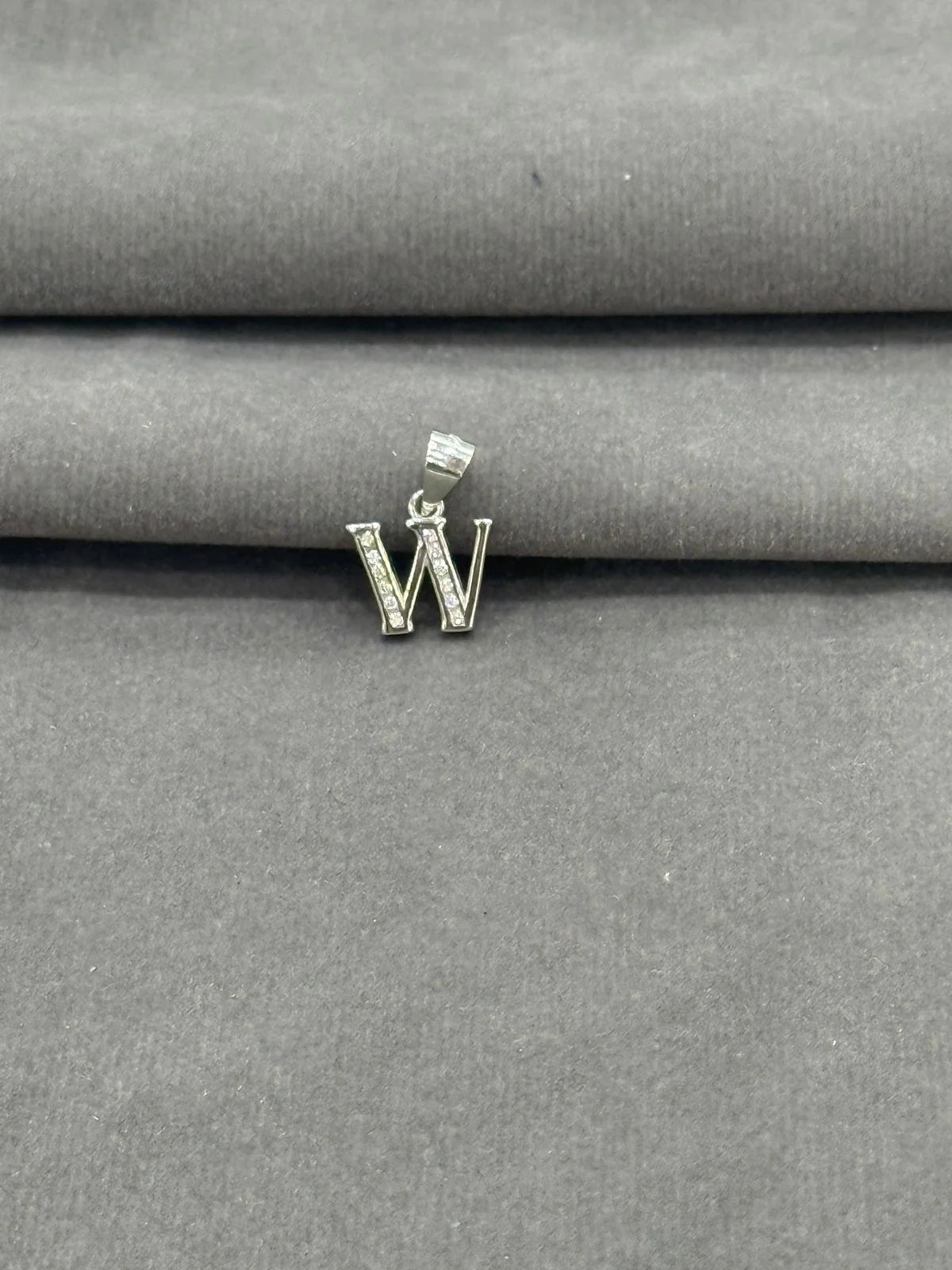 Silver 'W' pendant on a gray fabric background