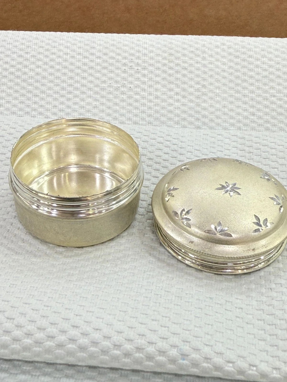 Silver jar with lid on a textured white surface