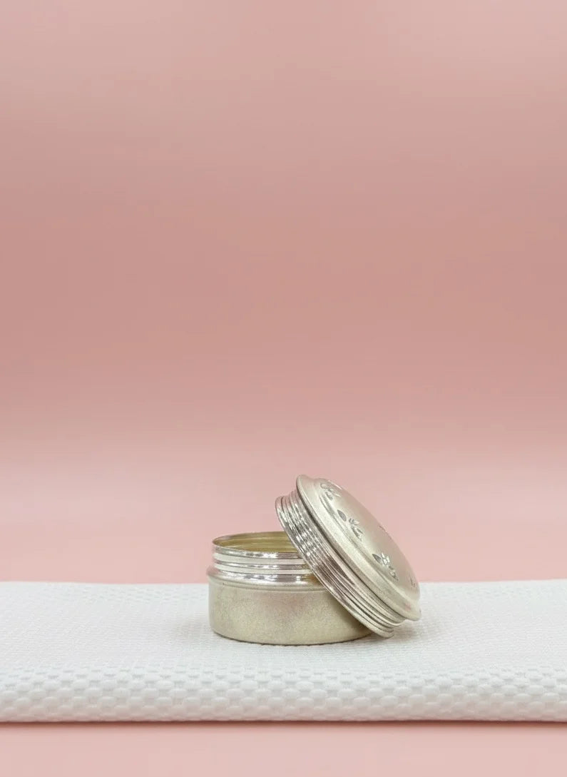 Silver cylindrical container with a white lid on a textured white surface against a pink background