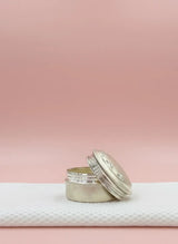 Silver cylindrical container with a white lid on a textured white surface against a pink background