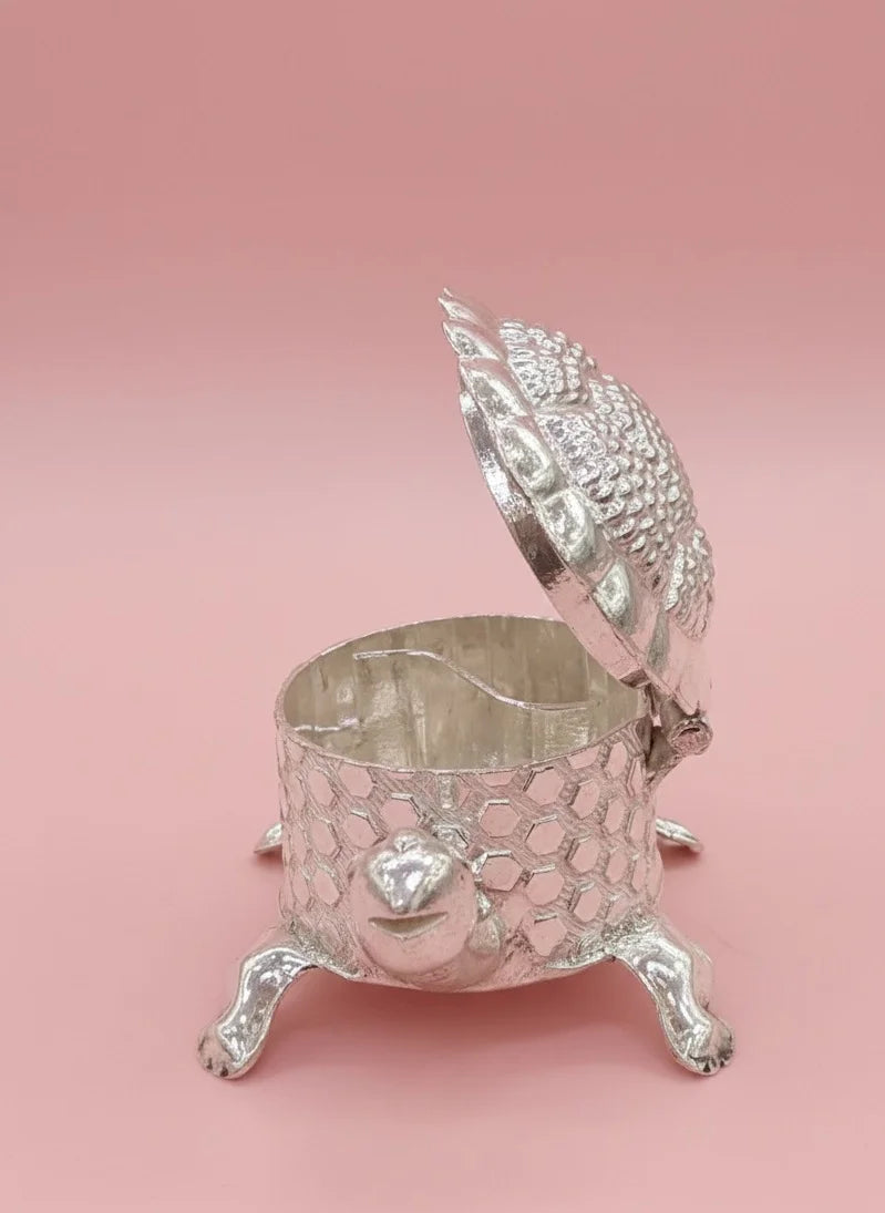 Silver decorative box with intricate design on a pink background