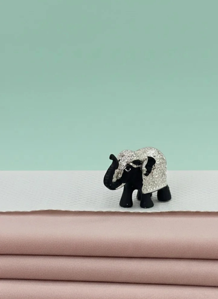 Small elephant figurine with decorative fabric on a stack of pink fabrics against a light green background
