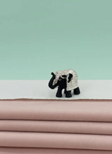Small elephant figurine with a decorative pattern on a stack of pink fabric against a light green background