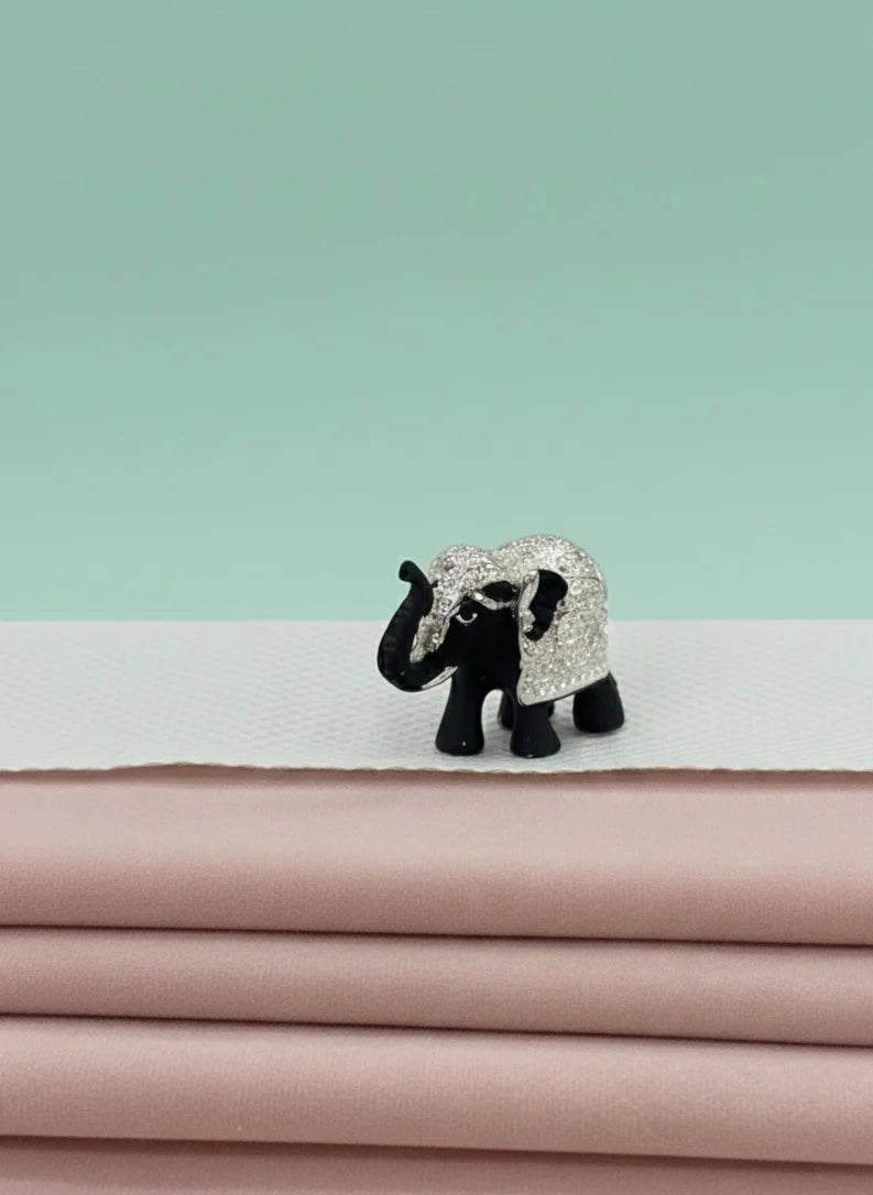 Small elephant figurine with a decorative pattern on a stack of pink fabric against a light green background