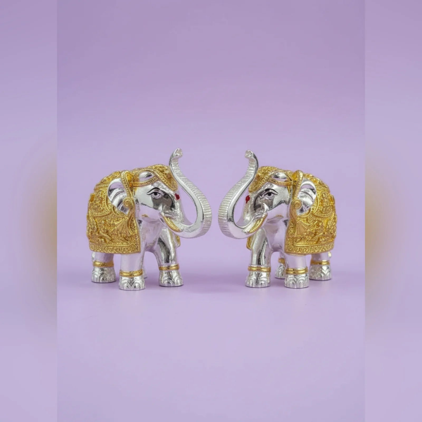 Decorative elephant figurines with gold and silver accents on a light purple background