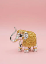 Decorative elephant figurine with gold and silver details on a pink background
