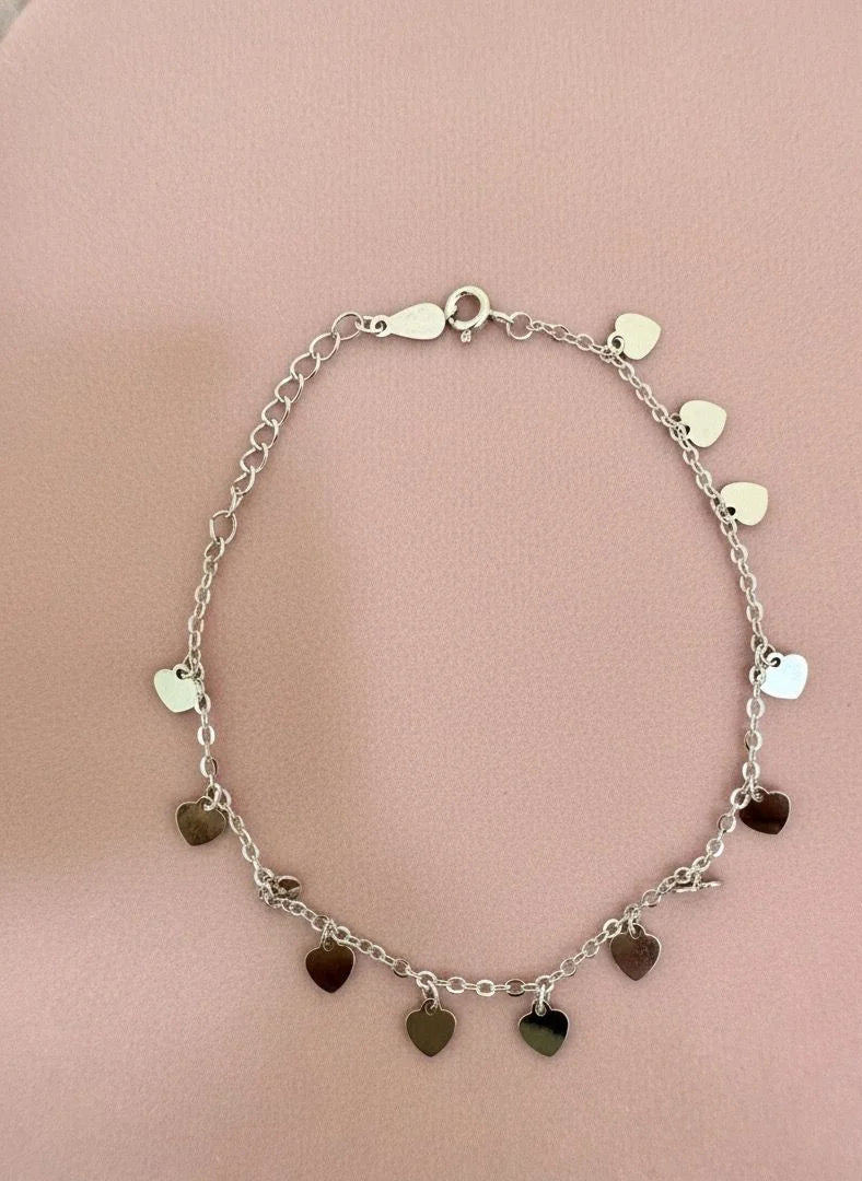 Silver bracelet with heart-shaped charms on a pink background