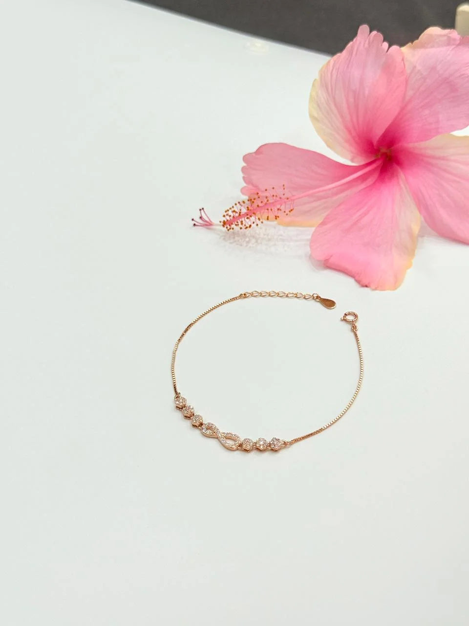 Rose gold bracelet on a light surface with a pink flower in the background