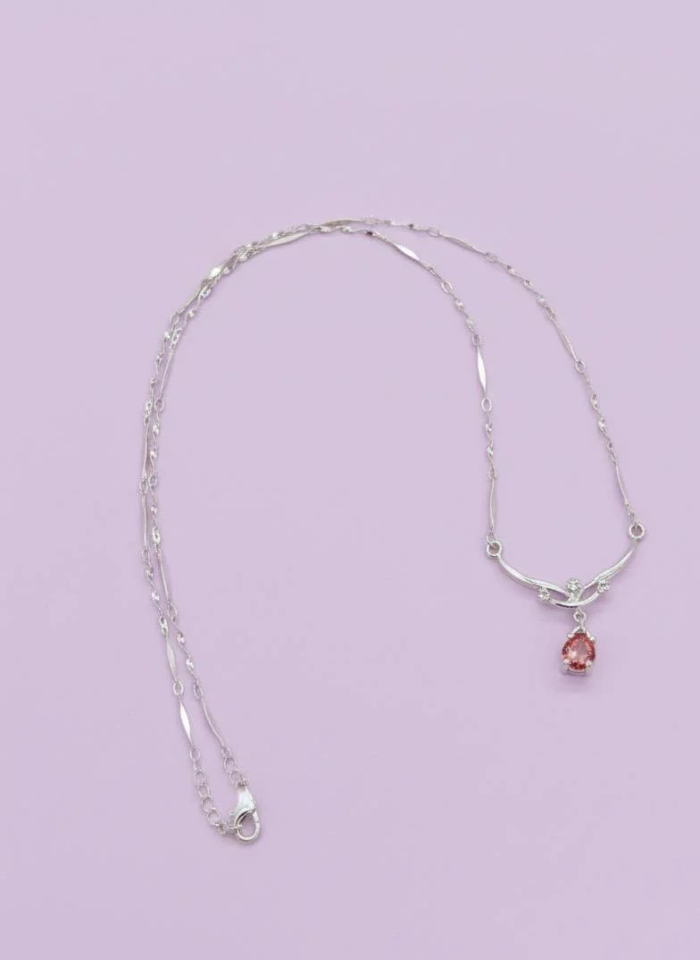 Silver necklace with a pink pendant on a light purple background