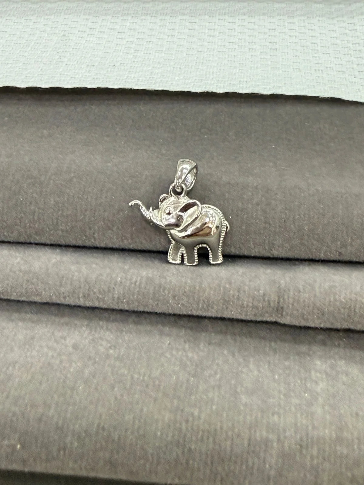Silver elephant pendant on a stack of gray fabric