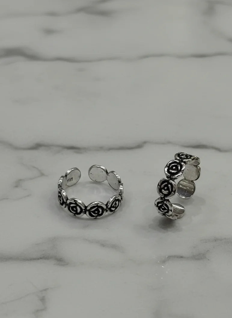 Silver toe rings with floral designs on a marble surface