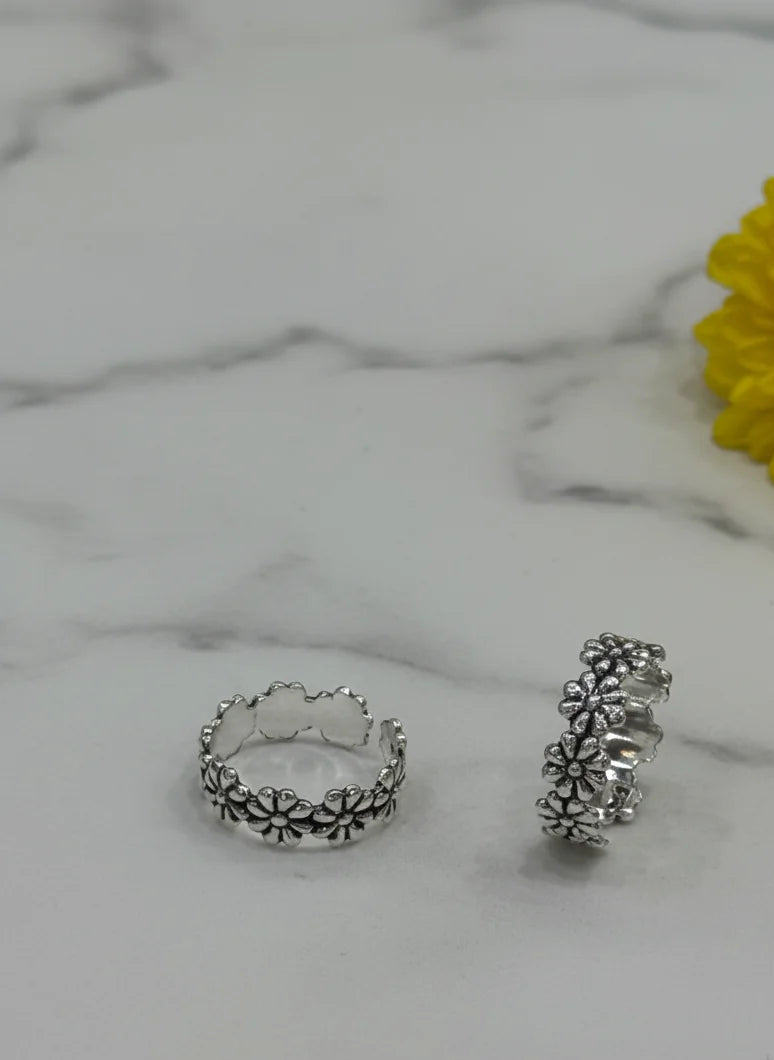 Two silver toe rings on a marble surface with a yellow flower.