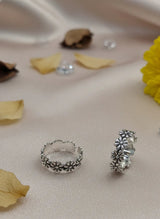 Silver toe rings on a soft fabric background with flowers and leaves.