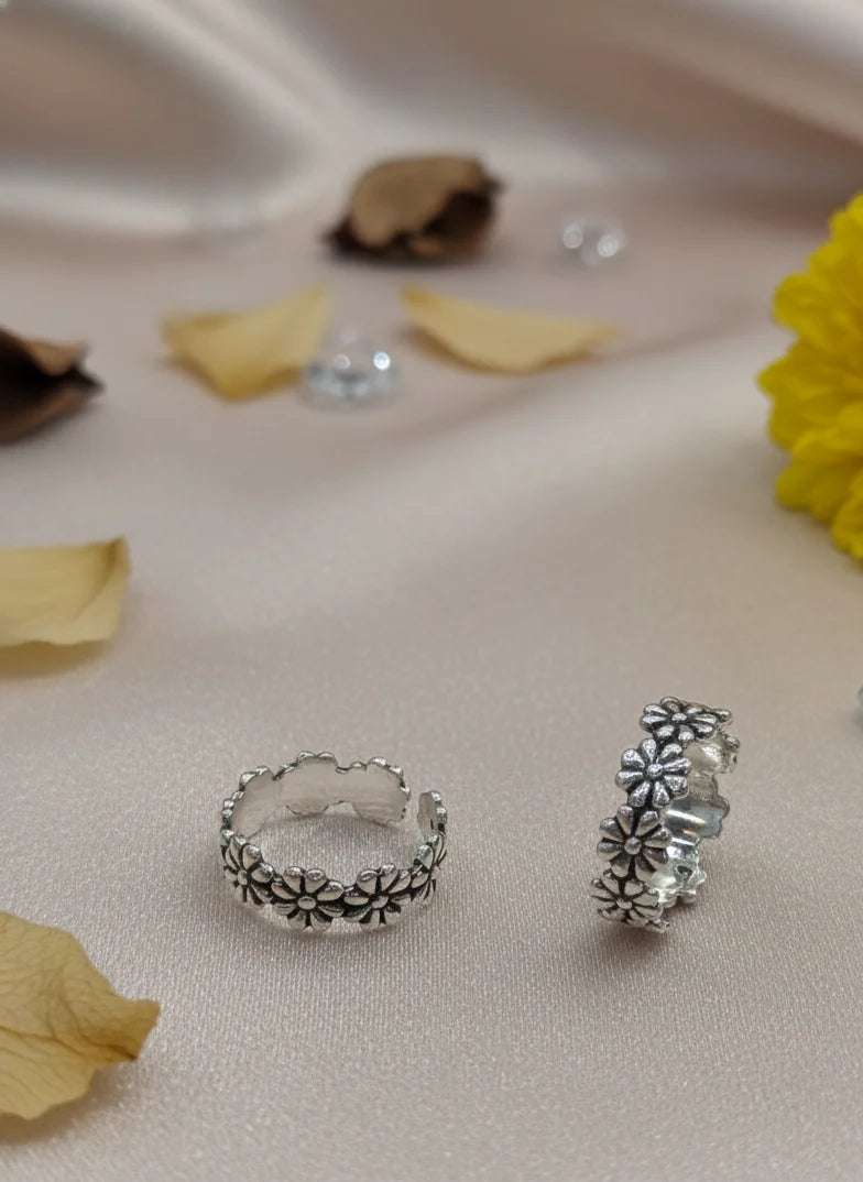 Silver toe rings on a soft fabric background with flowers and leaves.
