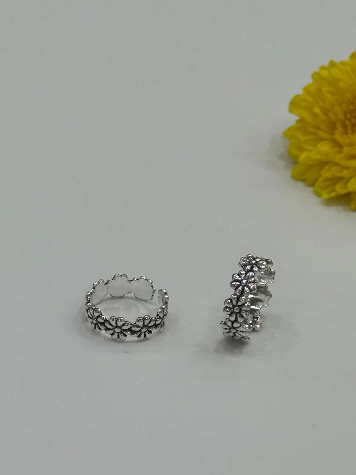 Two silver toe rings on a light gray background with a yellow flower.