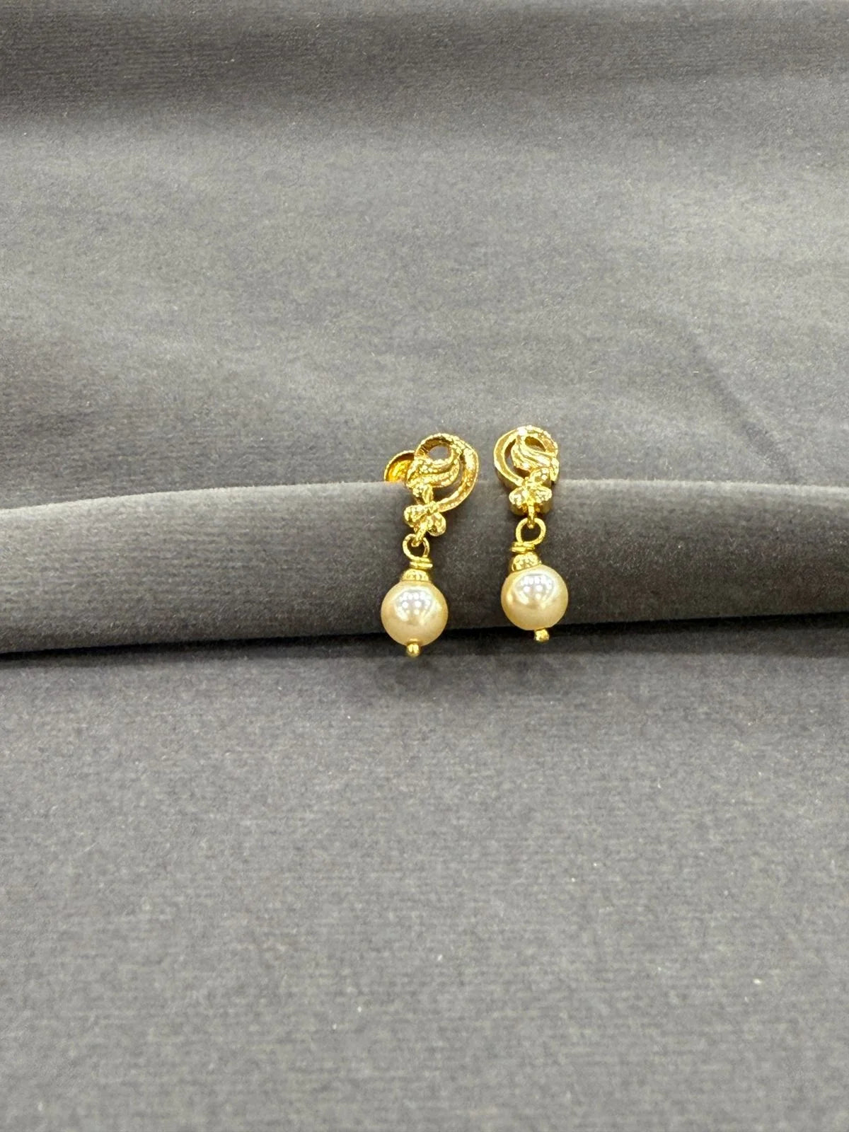 Gold earrings with pearl drops on a gray fabric background