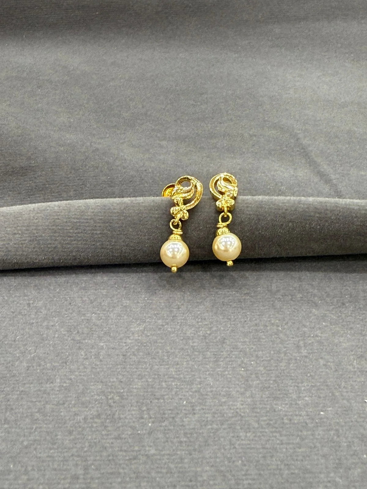 Gold earrings with pearl drops on a gray surface