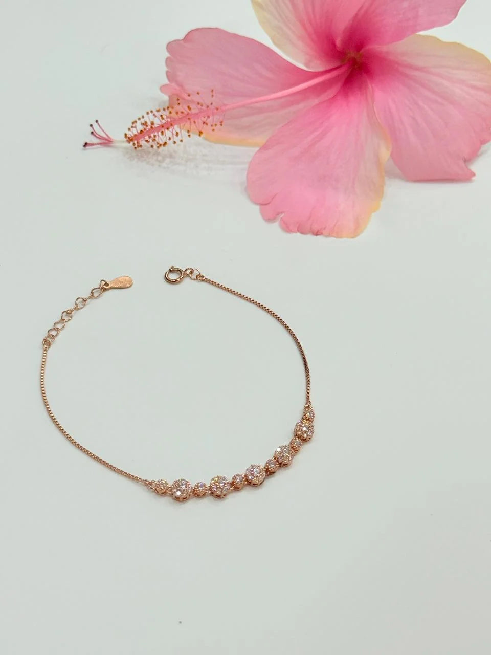Rose gold bracelet on a light gray background with a pink flower.