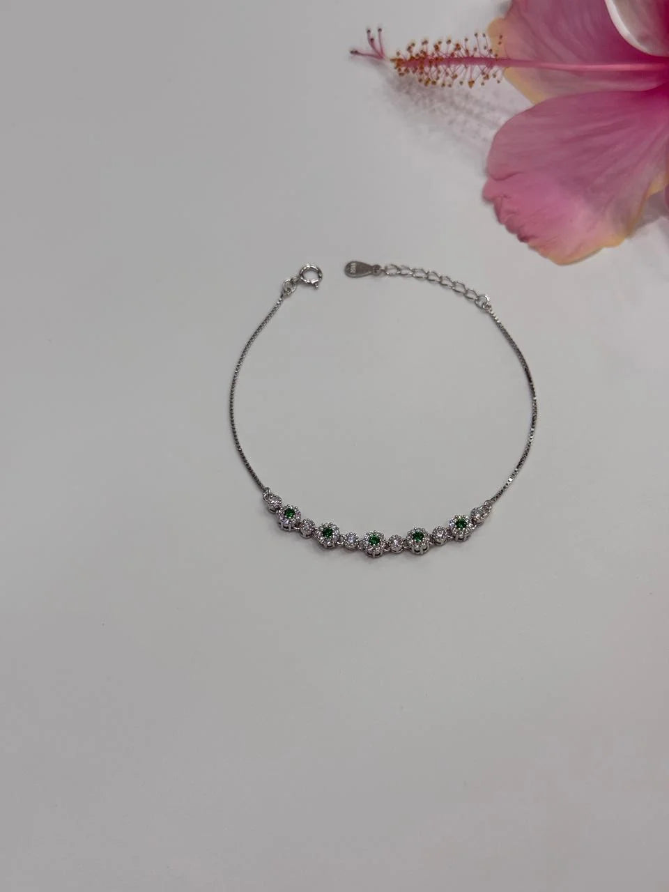Silver bracelet with green stones on a light gray background with a pink flower.