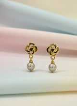 Gold earrings with pearl drops on a soft pastel background