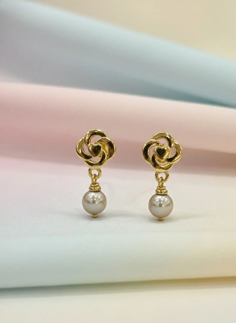Gold earrings with pearl drops on a soft pastel background