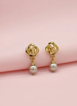 Gold earrings with pearl drops on a pink background