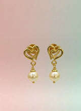 Gold heart-shaped earrings with pearl drops on a gradient background