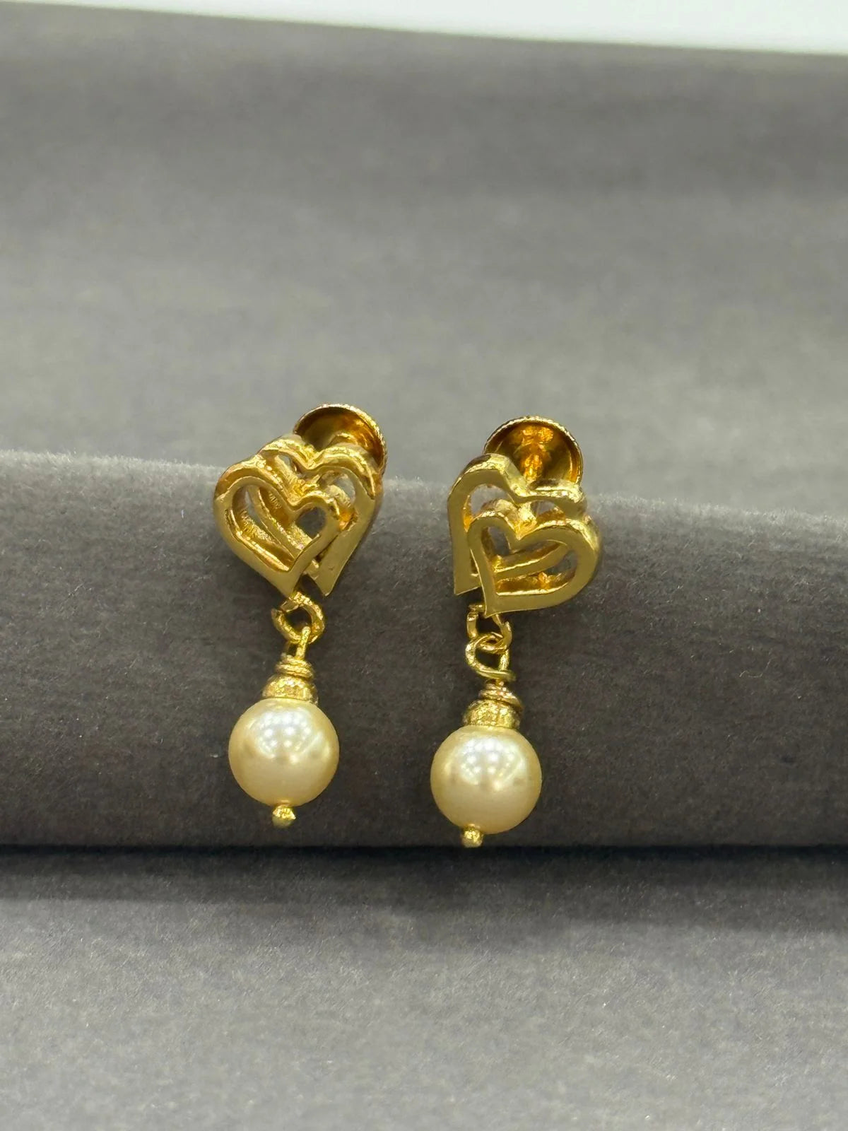 Gold earrings with pearl drops on a gray surface