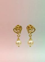 Gold heart-shaped earrings with pearl drops on a gradient background