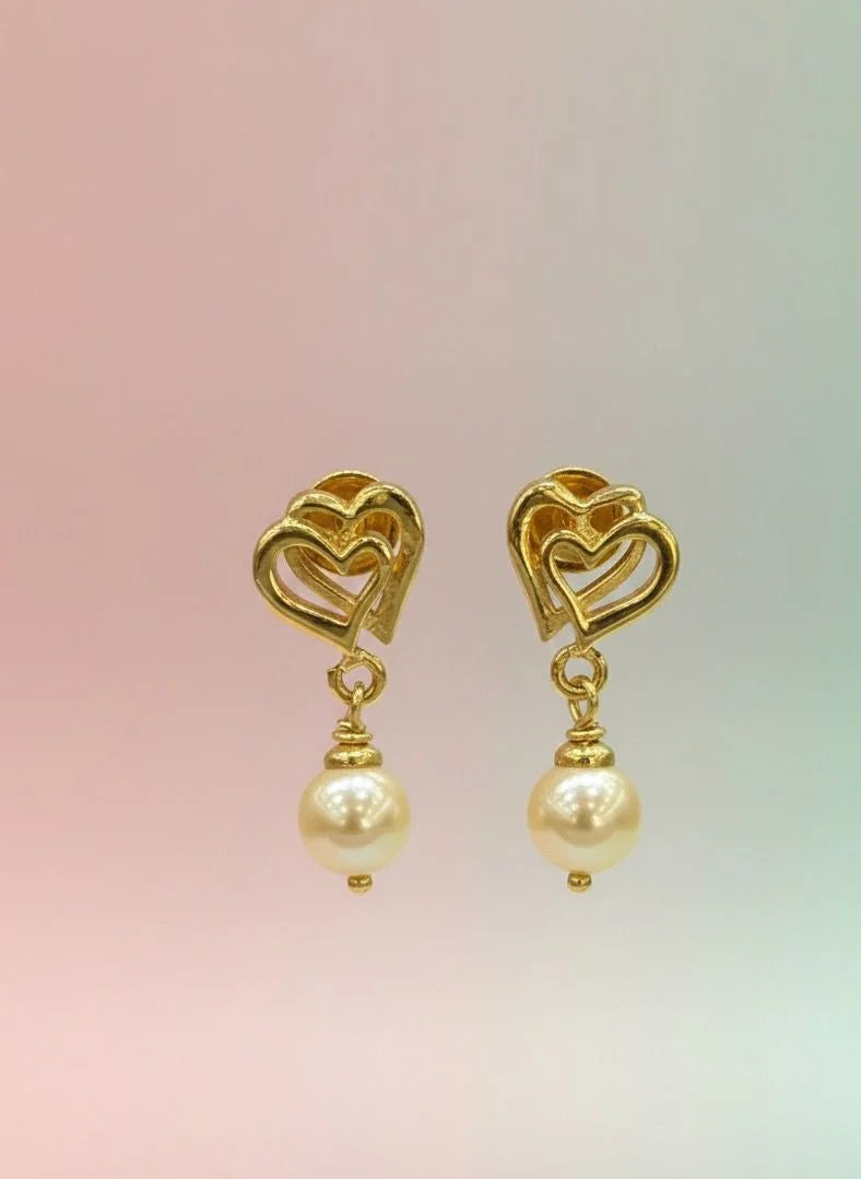 Gold heart-shaped earrings with pearl drops on a gradient background