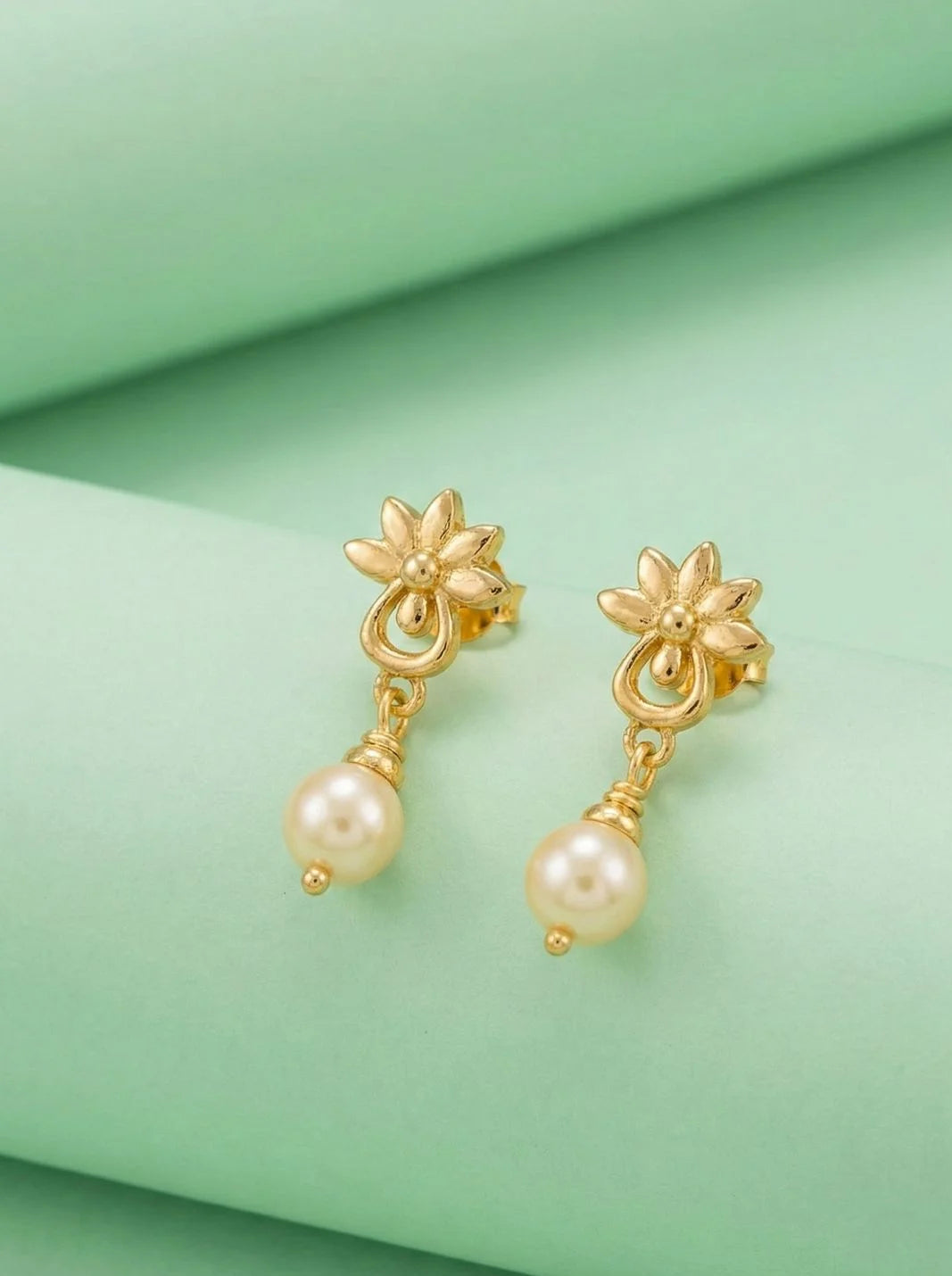 Gold earrings with pearl drops on a green fabric background