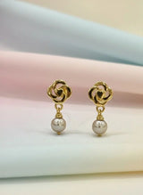 Gold earrings with pearl drops on a soft pastel background
