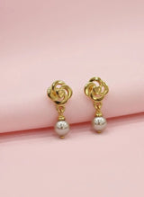 Gold earrings with pearl drops on a pink background