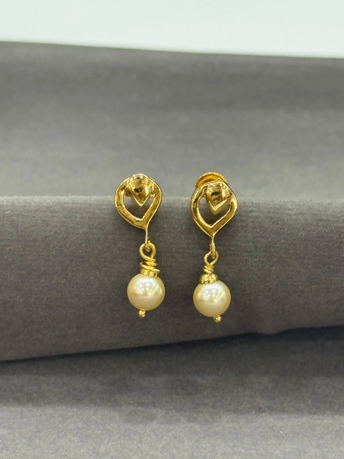 Gold earrings with pearl drops on a gray surface