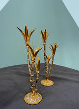 Two gold decorative plant stands on a dark surface with a light blue background