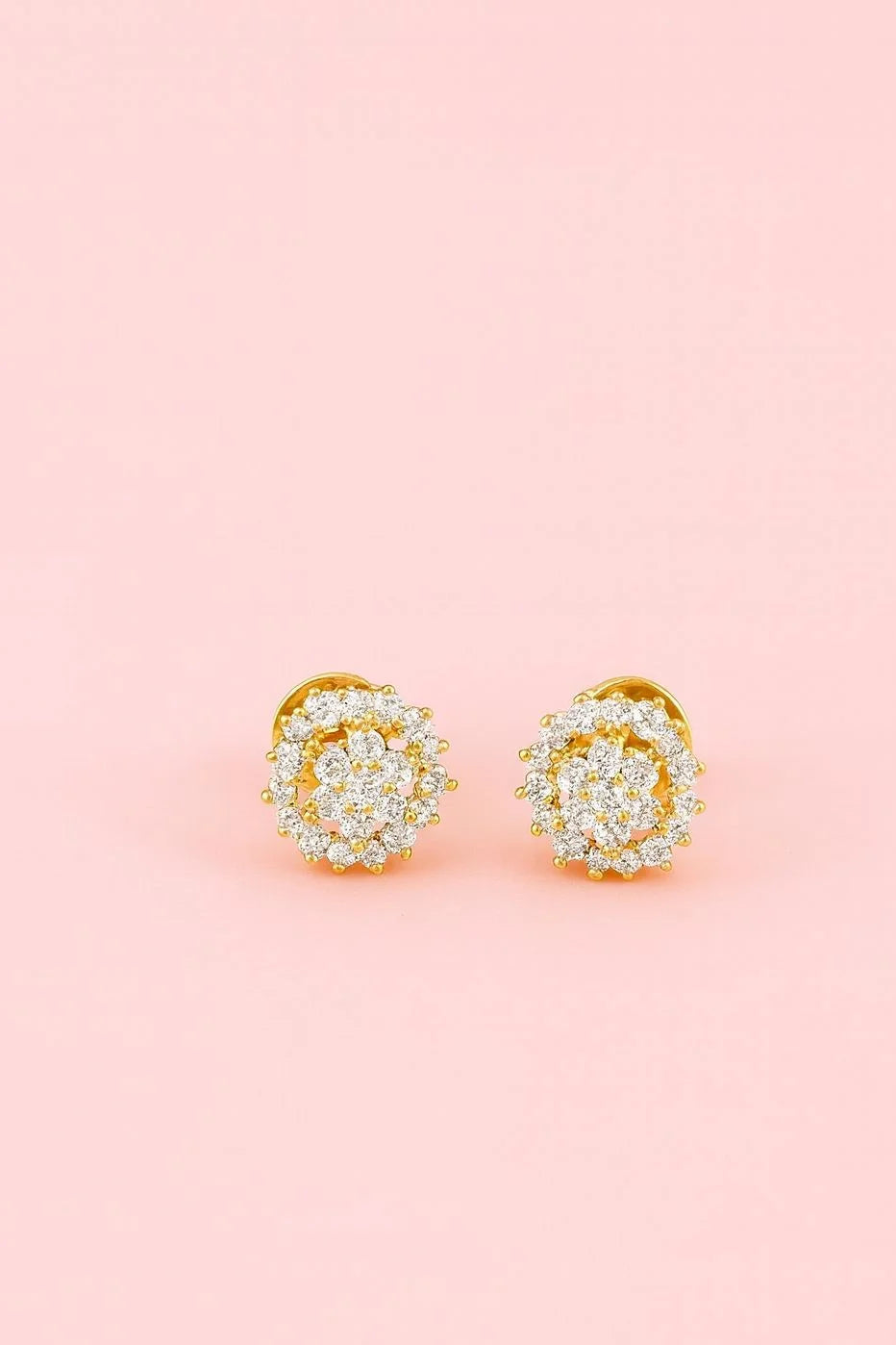 Gold earrings with diamond-like stones on a pink background