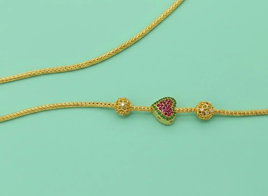 Gold mugappu chain with decorative beads on a light green background