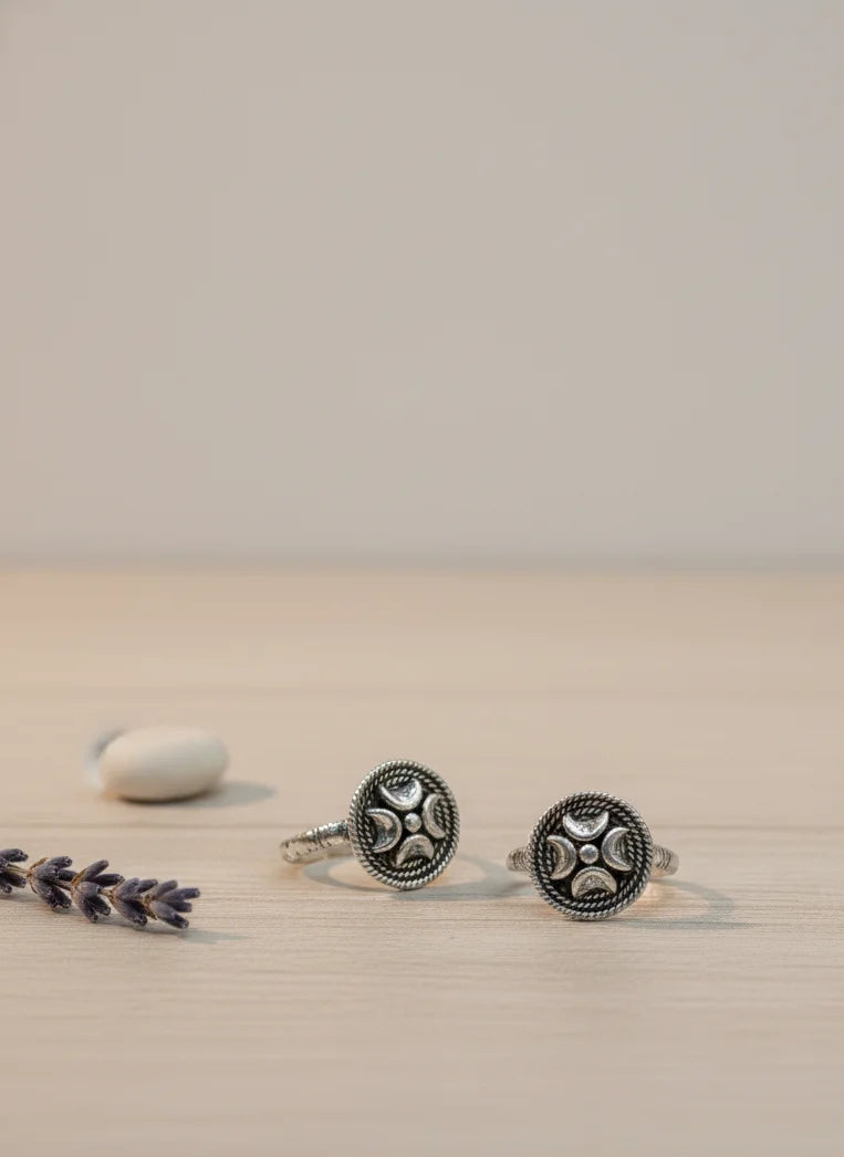 Silver toe rings with intricate designs on a beige surface with lavender.