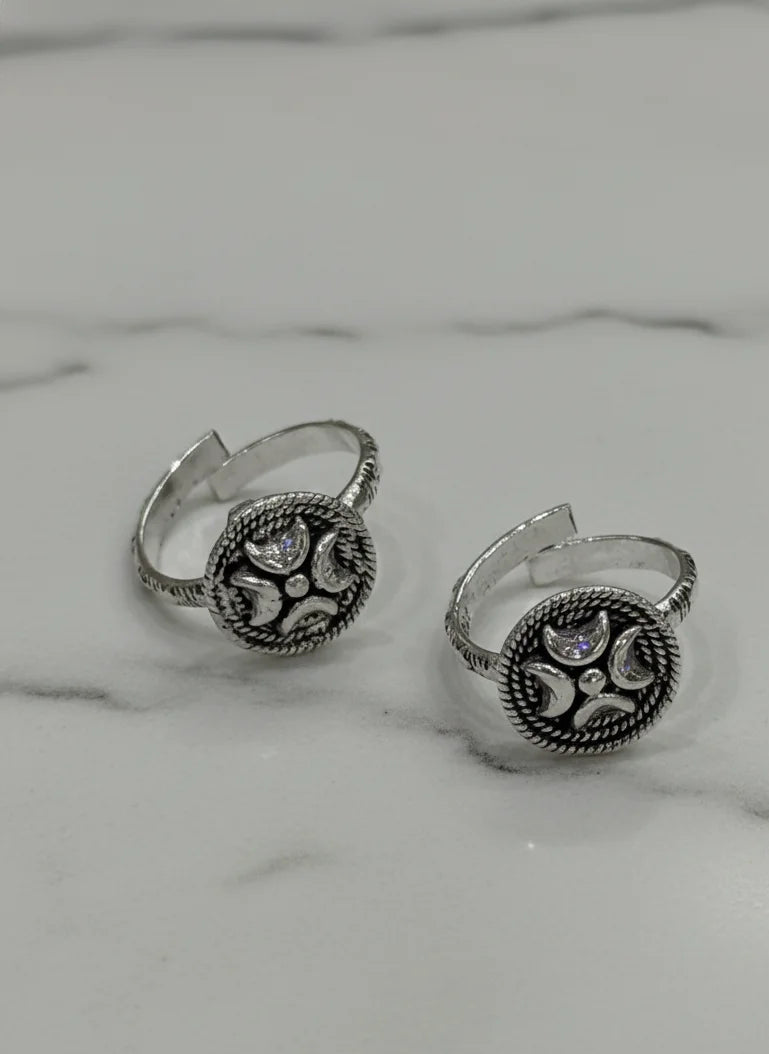 Pair of silver toe rings with intricate designs on a marble surface