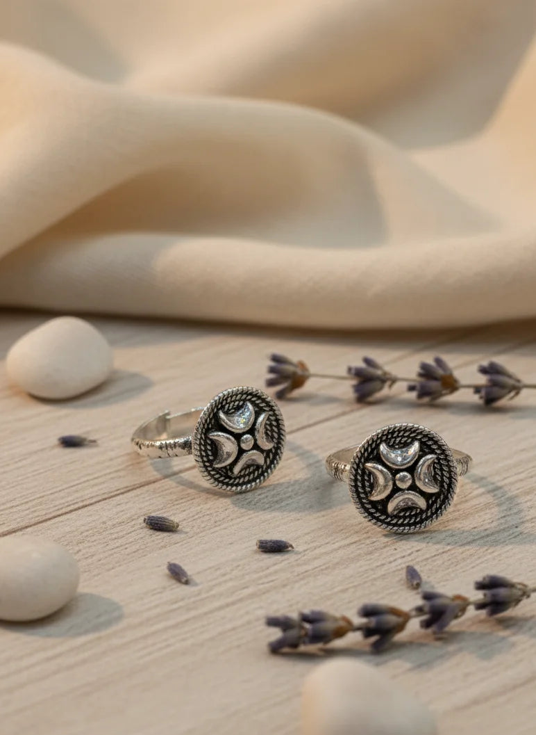 Two silver toe rings with intricate designs on a wooden surface with lavender and stones.