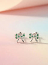 Bow-shaped earrings with green gemstones on a pastel pink and orange gradient background