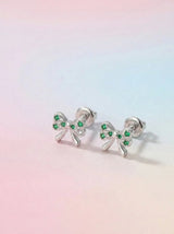 Bow-shaped earrings with green gemstones on a pastel gradient background